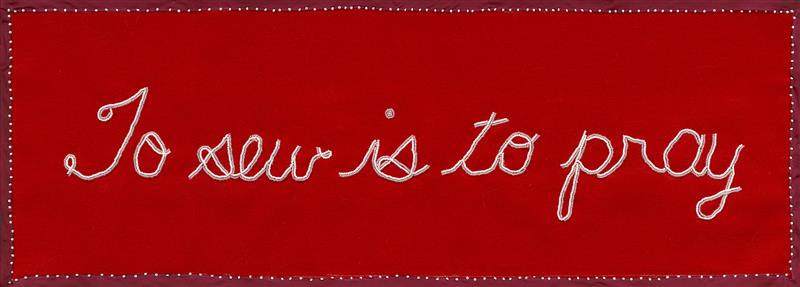 A red cloth with the words "to sew is to pray" sewn in white