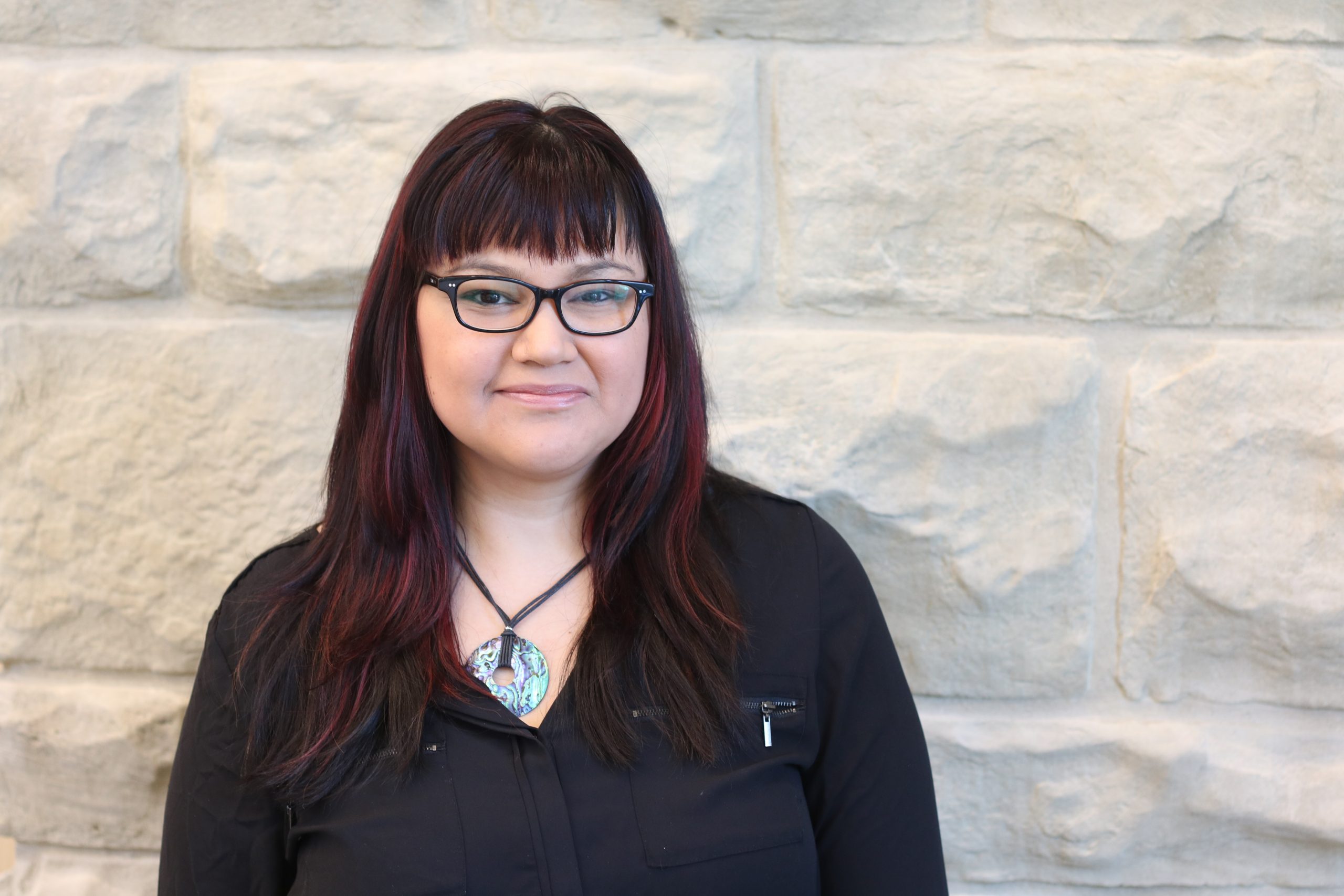 Image of Felicia standing in front of brick wall, staring into the camera.