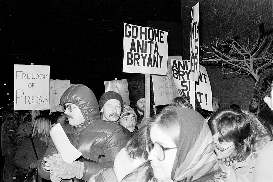 Black and white image featuring a protest. The image centres sign reading "Go Home Anita Bryant"