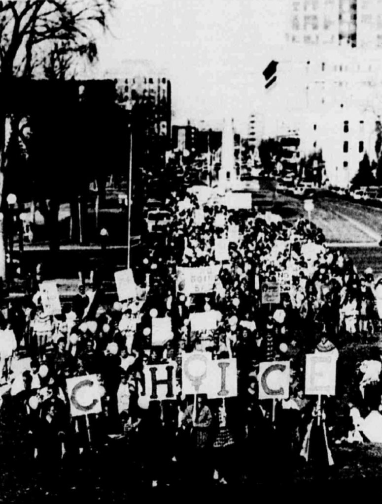 Black and white image of protest. Some protesters are holding posters spelling out the word CHOICE.