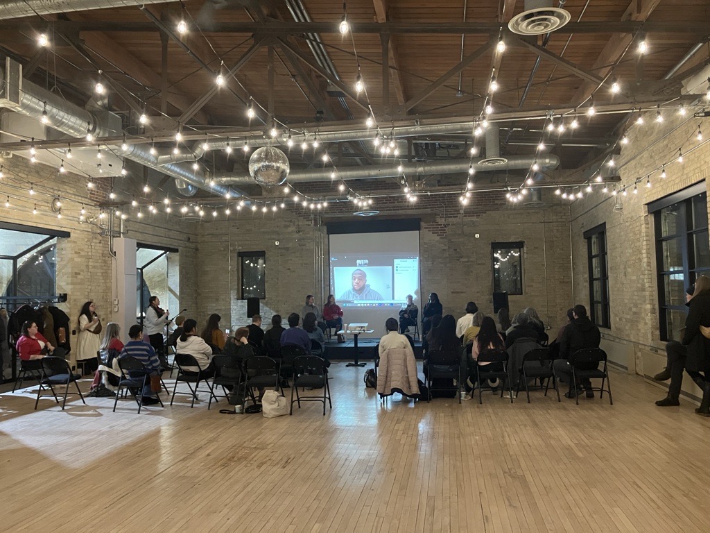 Image of a seated crowd watching a 4 people speak from the stage.