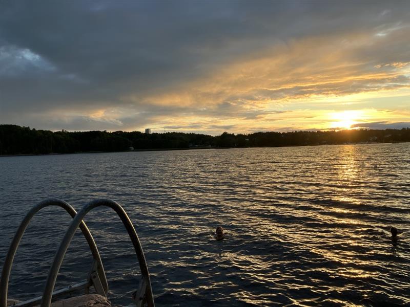 Image of the Baltic Sea with a sunset in the background and a ladder in the foreground. Two people are swimming in the water.