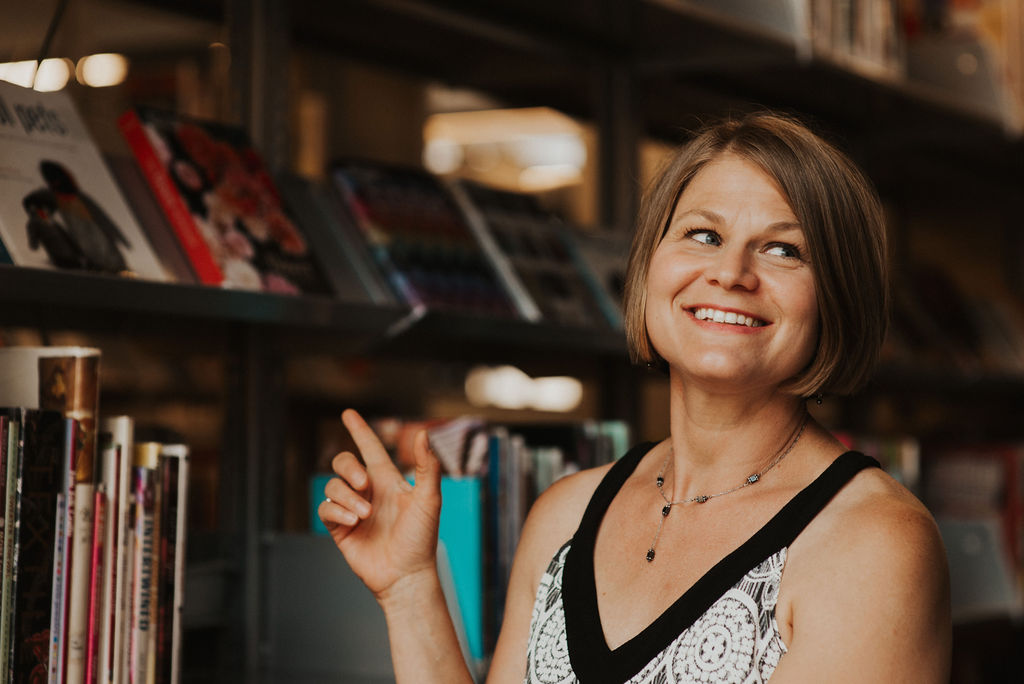 Headshot of Christine Stewart in front of a bookshelf, pointing to a book.